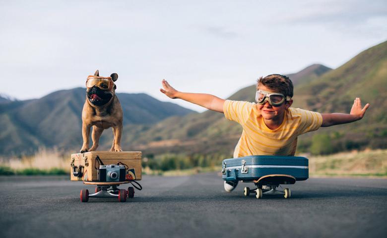 Boy and dog on skateboards with luggage, pretending to fly