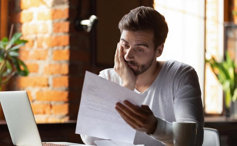 Concerned man reviewing a letter while sitting in front of a laptop