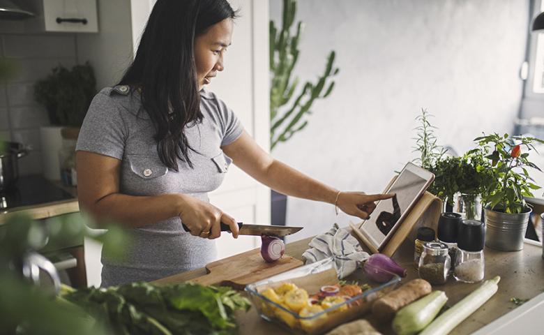 Woman cooking in her kitchen and referring to her tablet for the recipe