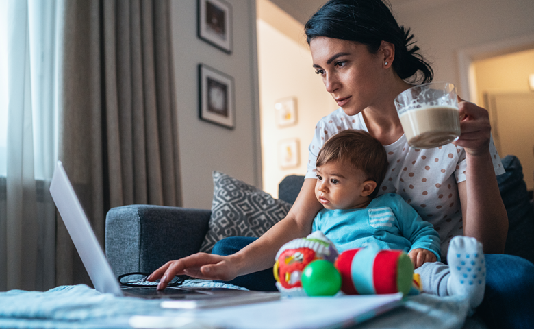 A mother uses her laptop while holding her baby