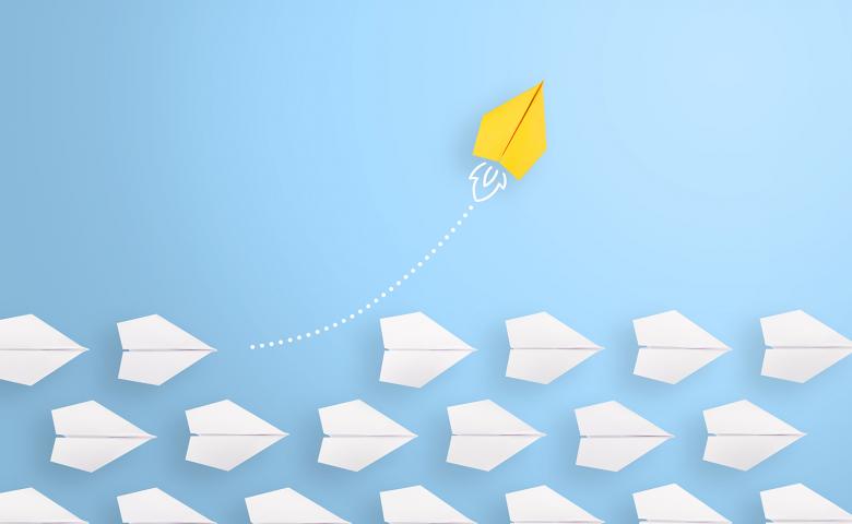 Series of white paper airplanes on a blue background with one yellow airplane flying its own route
