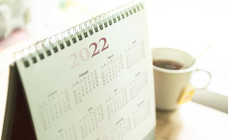 A coil bound, desktop calendar for 2022 sits next to a cup of coffee.