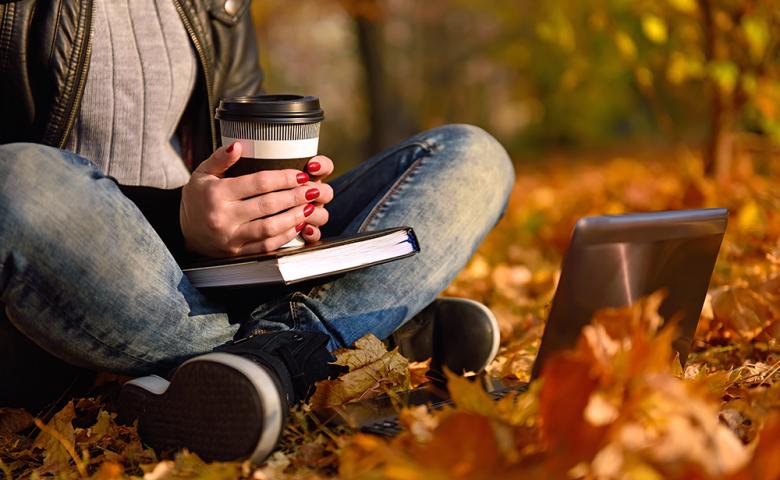 Face obscured girl with coffee cup sitting on leaves in park
