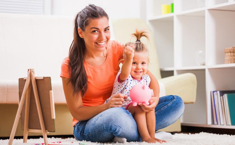 Mother and daughter sitting on floor with piggybank